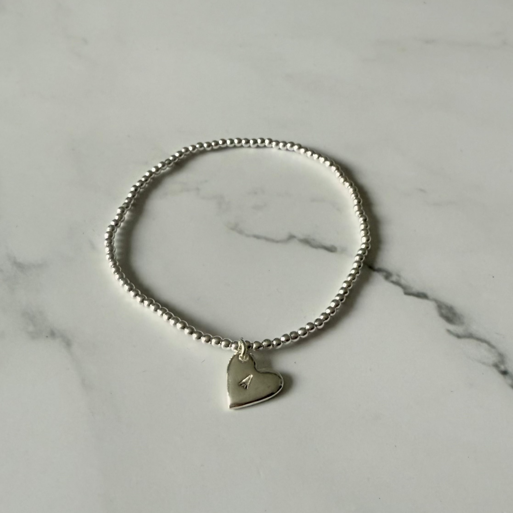 Silver bracelet with a heart-shaped tag on a marble surface